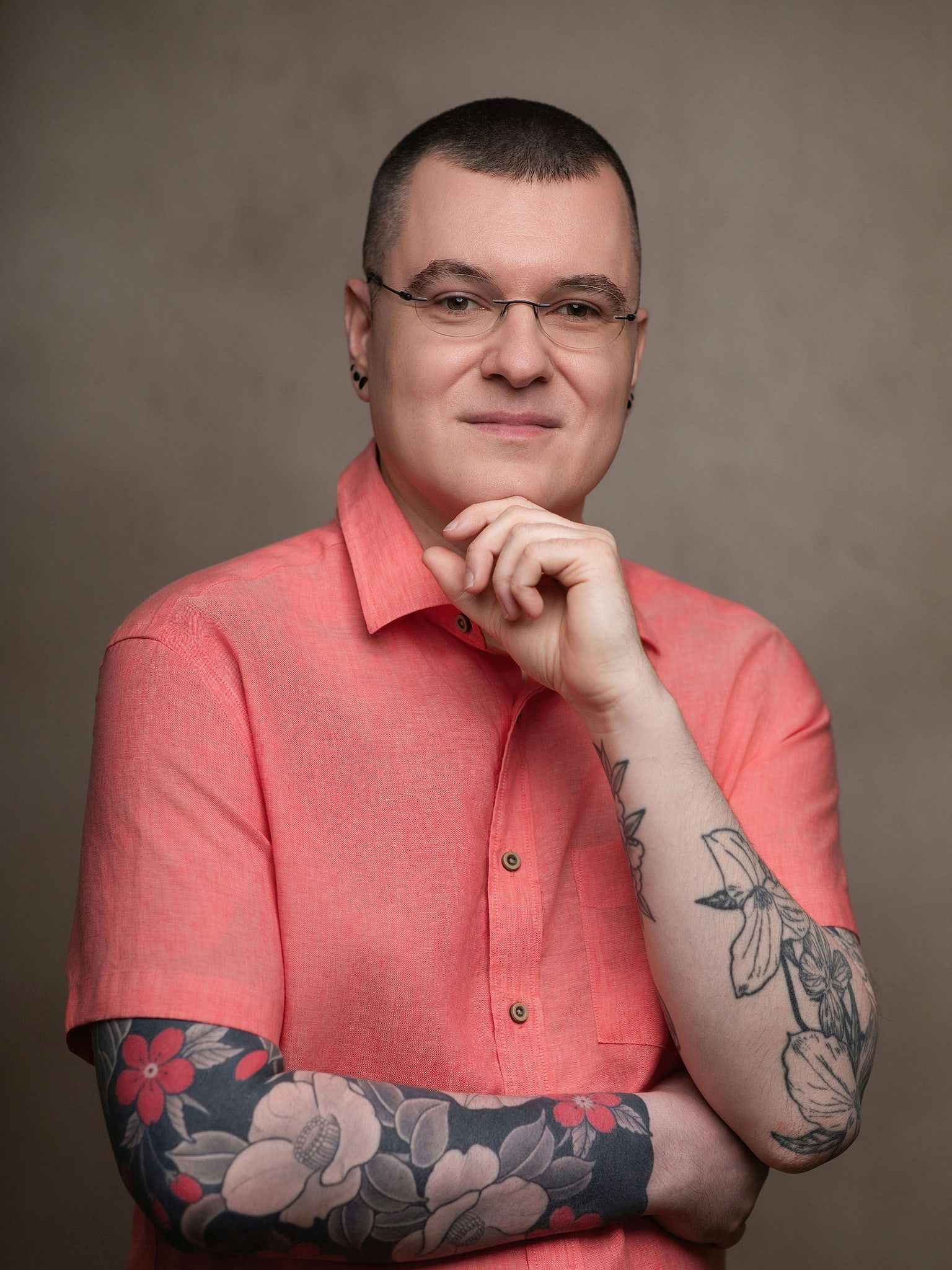 Kevin McElligott in a coral shirt, arms folded, with tattooed forearms